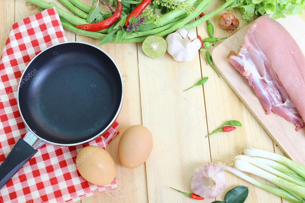 Pan and eggs on fabric, pork on chopping board and  vegetables on wood background with space for text, cooking concept
