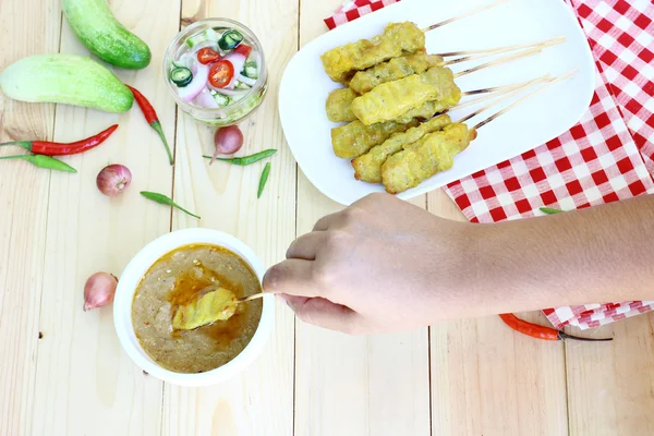 Kadınların elleri bir domuz eti satay tutarak vardır ve sosu daldırma