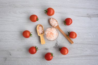 Renkli kaya tuzu ve saat şeklindeki domateslerin arka planında beyaz ahşap arka planda tahta kaşık var.