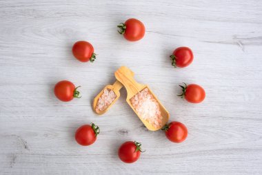 Renkli kaya tuzu ve saat şeklindeki domateslerin arka planında beyaz ahşap arka planda tahta kaşık var.