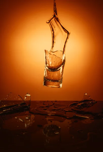 Exploderende glazen beker met water verpletterende over oranje achtergrond. — Stockfoto