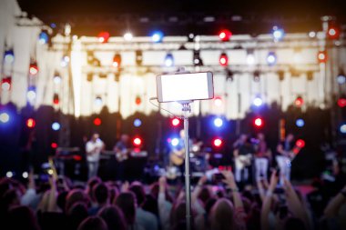 Müzik gösterisinde selfie çubuğunda akıllı telefon kullanmak. Resminiz için boş beyaz ekran.
