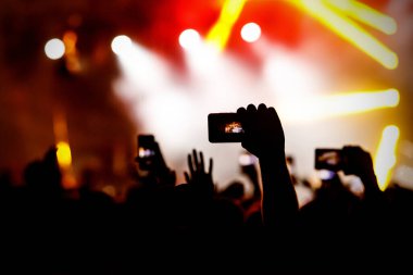 Canlı konserde fotoğraf ve video çekmek için kameralı telefon kullanan el silueti..