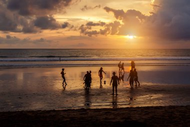 Kuta, Endonezya - 25 Mart 2019: Günbatımında futbol oynayan yerlilerin silueti.
