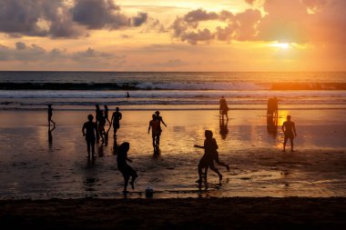Kuta, Endonezya - 25 Mart 2019: Günbatımında futbol oynayan yerlilerin silueti.