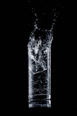 Siyah arka planda bardağa su sıçrar.