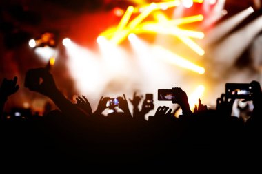 Konserde kalabalık. Eller ve akıllı telefonlar sahnenin önünde.