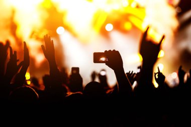 Konserde kalabalık. Eller ve akıllı telefonlar sahnenin önünde.