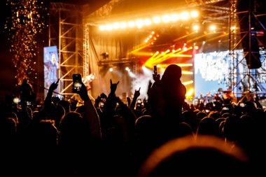 Konserde kalabalık. Eller ve akıllı telefonlar sahnenin önünde.