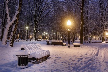 Şehir parkında karla kaplı bir bank. Kış manzarası