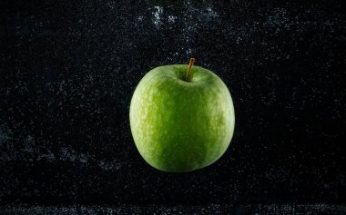 Siyah arkaplanda suya düşen yeşil elma.