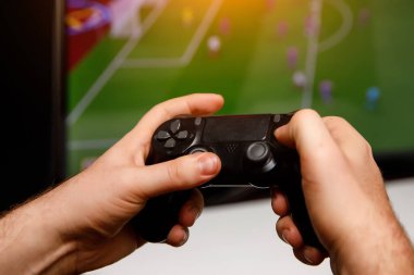 Man playing computer football or soccer game at home. Console controller in hands. clipart