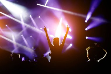 Ellerini kaldırmış bir kız silueti konserin ve müzik programının tadını çıkarıyor.