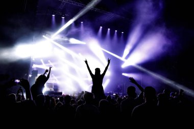 Ellerini kaldırmış bir kız silueti konserin ve müzik programının tadını çıkarıyor.