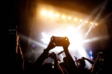 Bir sürü insan müzik festivalinde konser izlerken eğleniyor. Cep telefonlarıyla eller havaya.
