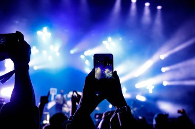 Bir sürü insan müzik festivalinde konser izlerken eğleniyor. Cep telefonlarıyla eller havaya.