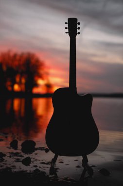 Gitar gün batımında göl kenarında.