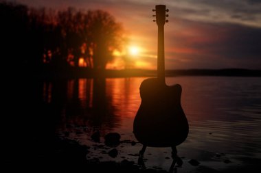 Gün batımında gitar silueti. Arka planda deniz ve ağaçlar