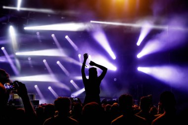 Ellerini kaldırmış bir kız silueti konserin ve müzik programının tadını çıkarıyor.