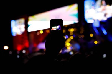 Akıllı telefonlu bir adam gece kulübündeki eğlence etkinliğinde cep telefonu fotoğrafı çekiyor.