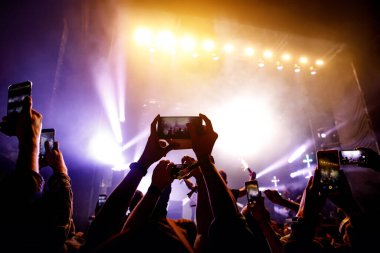 Bir sürü insan müzik festivalinde konser izlerken eğleniyor. Cep telefonlarıyla eller havaya.
