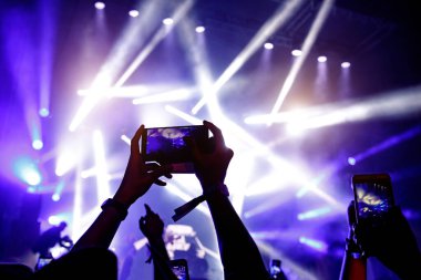 Bir sürü insan müzik festivalinde konser izlerken eğleniyor. Cep telefonlarıyla eller havaya.