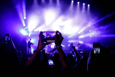 Bir sürü insan müzik festivalinde konser izlerken eğleniyor. Cep telefonlarıyla eller havaya.