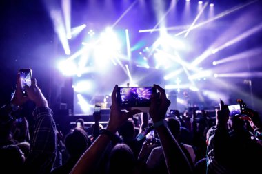 Bir sürü insan müzik festivalinde konser izlerken eğleniyor. Cep telefonlarıyla eller havaya.