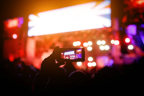 Silhouette of hands with a smartphone at a big music festival, video recording of stage show