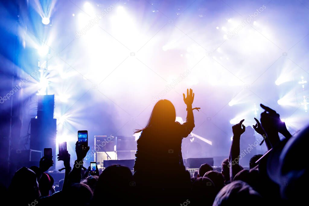 The audience at the concert enjoys. Silhouettes of raised hands and smartphones