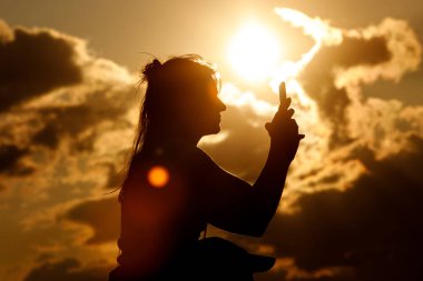 Yaz günbatımında bir kızın silueti. Müzik festivalini cep telefonuyla İnternet 'e aktar