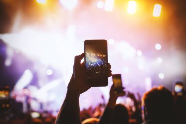 Sahne ışıklarının önündeki bir konserde cep telefonuyla fotoğraf çekmek.