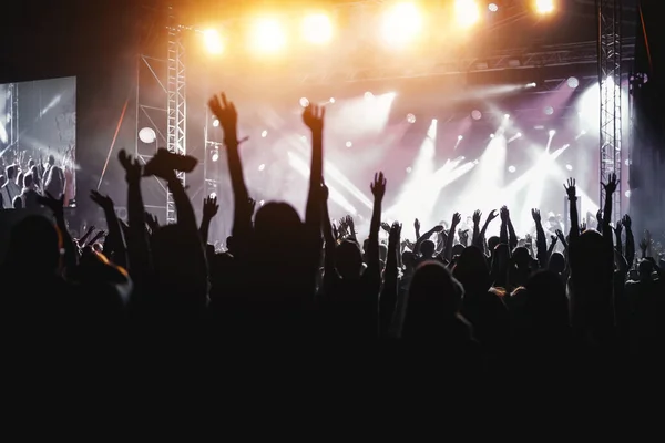 People with raised hands, silhouettes of concert crowd in front of bright stage lights