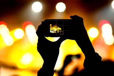 Akıllı telefon elinde, konser sahnesini çekiyor.