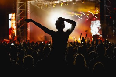 Müzik konserinde elini kaldırmış bir kız silueti..