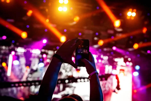 Hand with the smartphone turned on to record or take pictures during the live concert