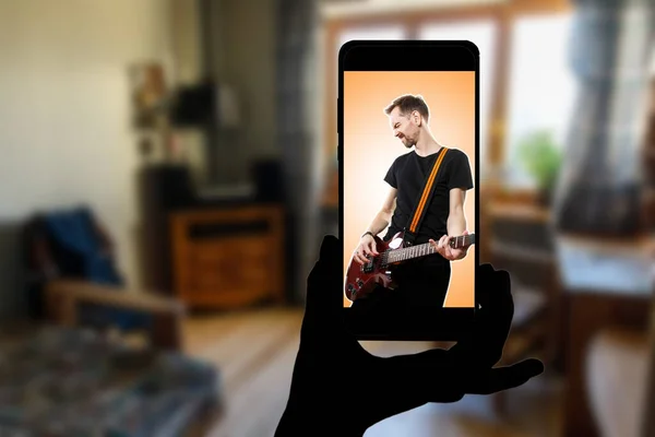 Watching online concert at home. Singer with a guitar on the screen of the smartphone.