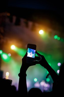 Akıllı telefon kayıtlarıyla el silueti canlı müzik festivalinde konser sahnesinin fotoğrafını çekiyor.
