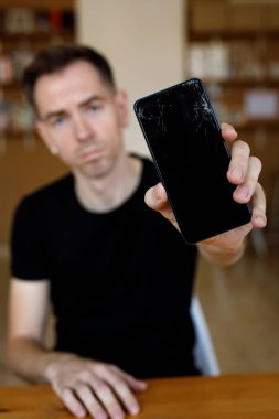 Üzgün adam elinde kırık bir akıllı telefon tutuyor.