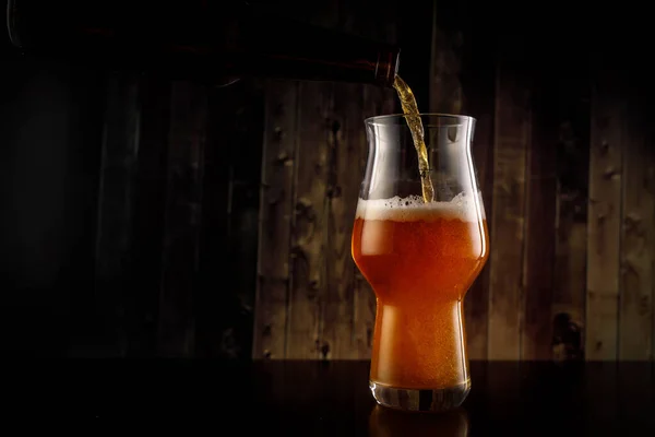 Versare la birra nel bicchiere dalla bottiglia su sfondo di legno. — Foto Stock