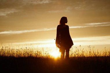 Gün batımında mutlu genç bir kadının silueti, ekose pançolu açık hava kızı.