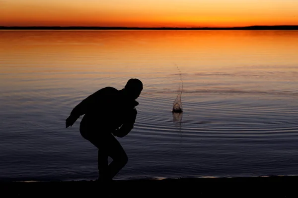 Silhouet Van Een Man Gooit Stenen Het Meer Bij Zonsondergang — Stockfoto