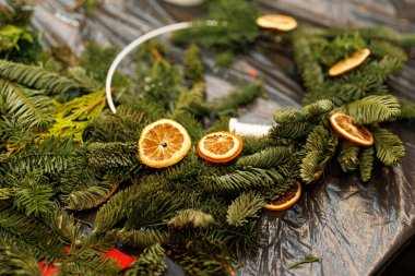 Yeşil köknar dalları ve Noel çelengi yapımında kullanılan kurutulmuş portakal dilimleri olan bir masa..