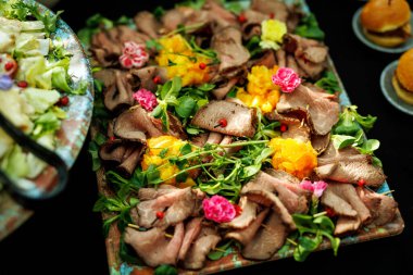 Dilimlenmiş biftek, yenilebilir çiçekler ve narenciye ile süslenmiş. Yemek servisi, gurme mutfağı ya da yemek tasarımı için uygun.