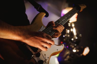 Elektrikli gitarist, parlak kıyafetli bulanık bir şarkıcıyla sahnede. Müzik, konser ve gece hayatı temalarına uyuyor.