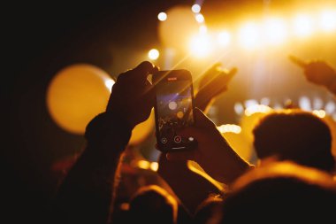 Kalabalığın üstünde tutulan akıllı telefonun yakın çekimi, beyaz balonlar ve parlak ışıklarla bir konser kaydı..