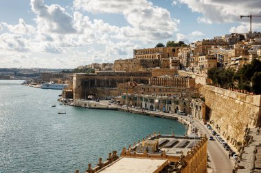 Saint Angelo Kalesi ve Valletta 'nın panoramik manzarası bulutlu gökyüzünün altında mavi deniz boyunca yükseliyor. Seyahat, miras ve mimari temalar için harika.