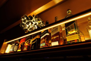 Kaliteli viski şişeleri, sıcak ışıklandırma altında altın bir bar rafında sergileniyor. Barın içini, gece hayatını ya da lüks içecek temalarını göstermek için mükemmel..