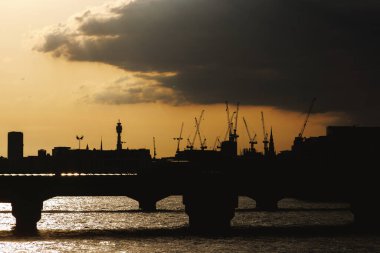 Londra şehir silueti, vinçler, BT Kulesi ve Thames Nehri üzerinde turuncu bir akşam gökyüzüne bakan binalar..