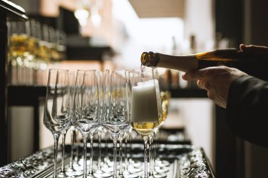 Parti hazırlıkları sırasında boş flütlerle çevrili bir bardağa köpüklü şarap dolduruyorum..